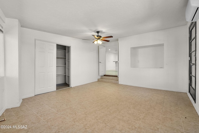 unfurnished bedroom with a textured ceiling, a wall mounted air conditioner, ceiling fan, and a closet