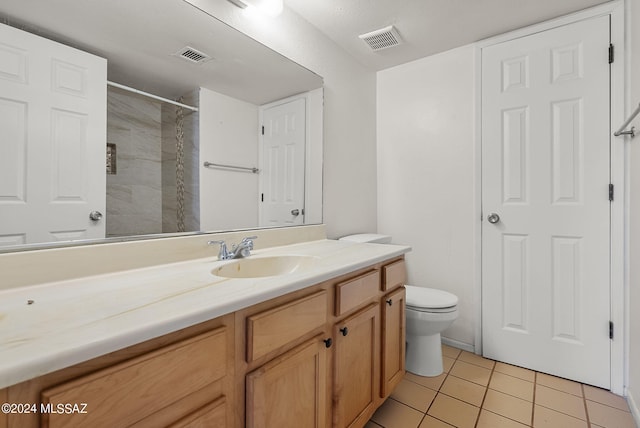 bathroom with vanity, toilet, a tile shower, and tile patterned floors