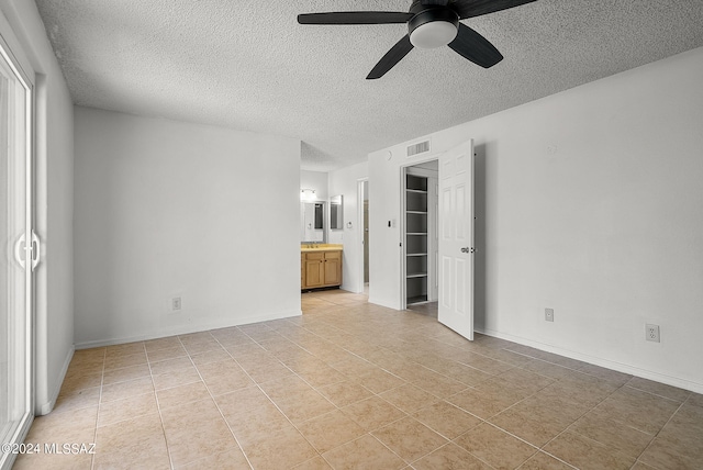 unfurnished bedroom featuring ensuite bathroom, a closet, a spacious closet, ceiling fan, and a textured ceiling