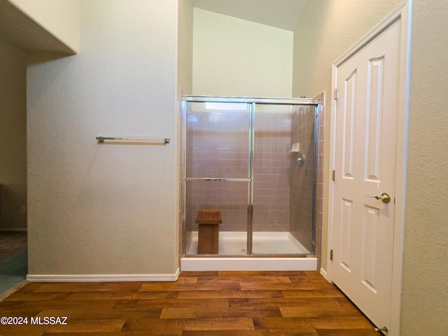 bathroom with a shower with door, vaulted ceiling, and wood-type flooring