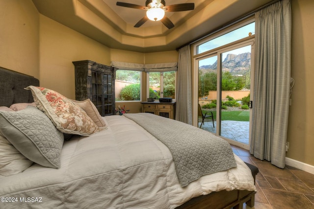 bedroom featuring a ceiling fan, baseboards, access to exterior, a raised ceiling, and a mountain view