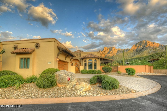mediterranean / spanish home featuring a garage, decorative driveway, stucco siding, a tiled roof, and a mountain view