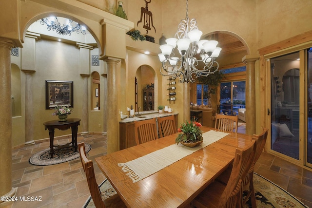 dining space featuring decorative columns, a towering ceiling, arched walkways, an inviting chandelier, and stone tile floors