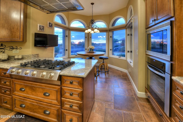 kitchen featuring extractor fan, appliances with stainless steel finishes, hanging light fixtures, a notable chandelier, and light stone counters