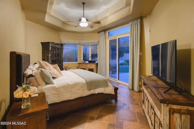 bedroom featuring ceiling fan, stone finish flooring, a tray ceiling, and access to outside