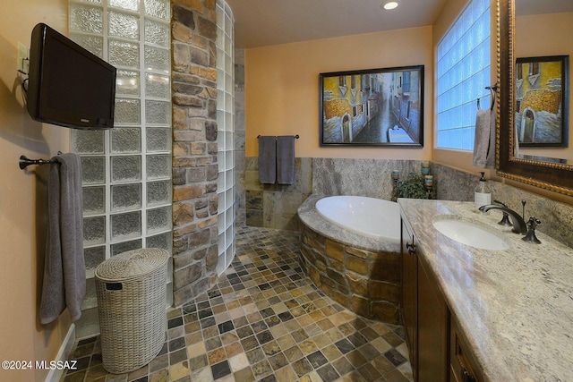 full bath featuring stone finish flooring, a bath, tile walls, walk in shower, and vanity