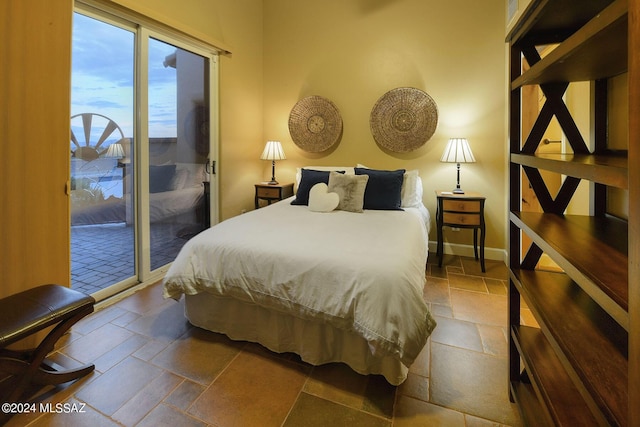 bedroom featuring stone tile floors, baseboards, and access to outside