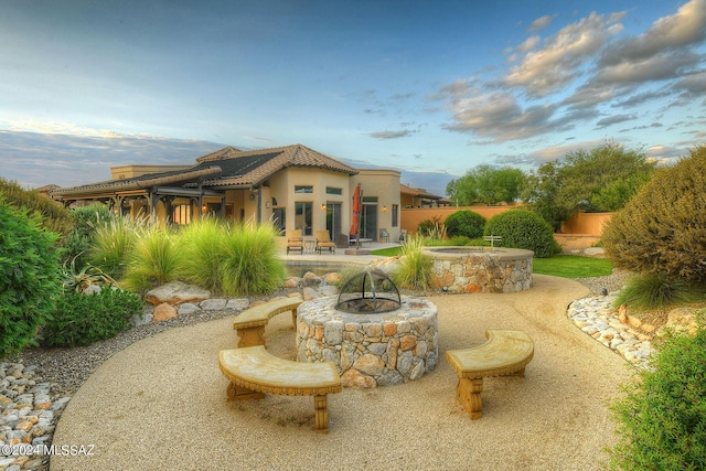 back of property with a patio, an outdoor fire pit, an in ground hot tub, stucco siding, and a tiled roof