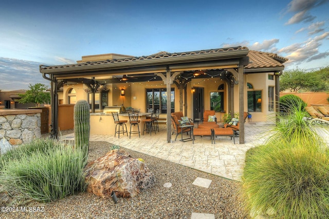 back of house featuring a patio area, stucco siding, a tile roof, and outdoor dry bar
