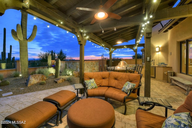 patio terrace at dusk featuring a fenced backyard, a ceiling fan, an outdoor living space, and exterior kitchen