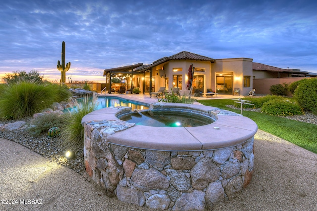 pool at dusk with a patio and an in ground hot tub