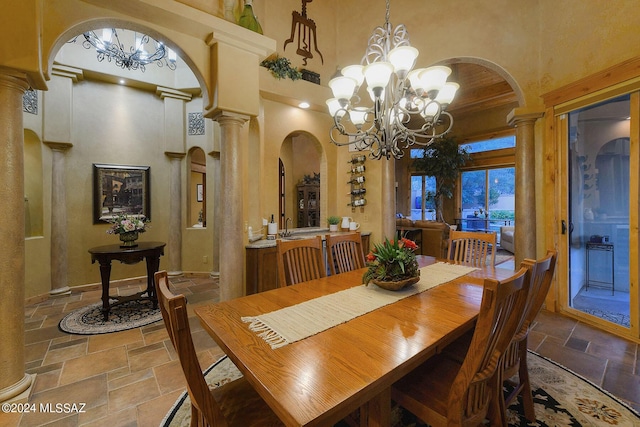 dining room featuring decorative columns, arched walkways, a notable chandelier, a high ceiling, and stone tile floors