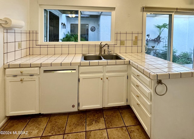 kitchen with white dishwasher, tile counters, white cabinets, and tasteful backsplash