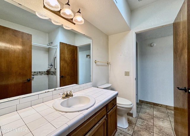 bathroom featuring vanity, tile patterned flooring, toilet, a textured ceiling, and tiled shower