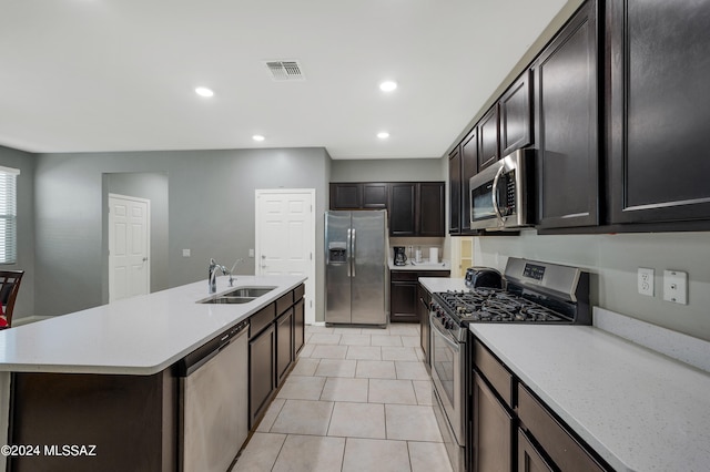 kitchen with a kitchen island with sink, dark brown cabinets, light tile patterned floors, sink, and appliances with stainless steel finishes