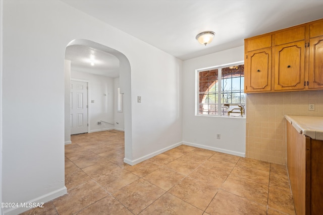 kitchen featuring arched walkways, tile countertops, baseboards, and brown cabinetry