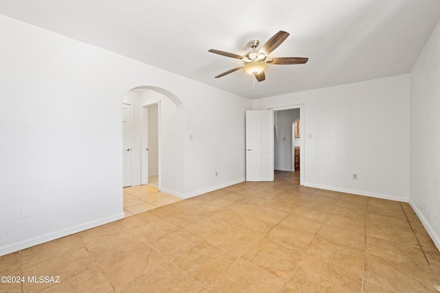 unfurnished room with arched walkways, light tile patterned floors, baseboards, and ceiling fan