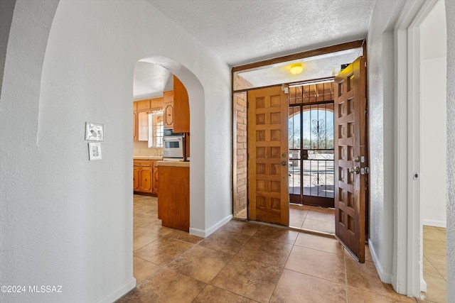 foyer featuring a textured ceiling, plenty of natural light, light tile patterned flooring, and sink