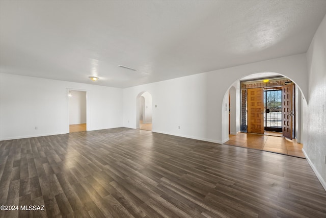 unfurnished room with arched walkways, wood finished floors, baseboards, and visible vents