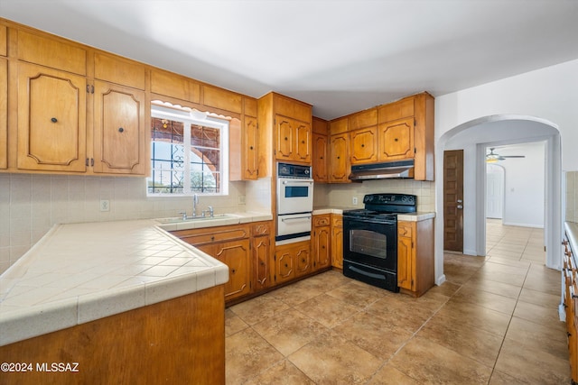 kitchen featuring white oven, a warming drawer, under cabinet range hood, a sink, and black range with electric cooktop