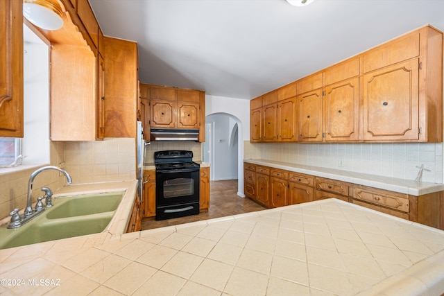 kitchen featuring black electric range, kitchen peninsula, sink, and tasteful backsplash