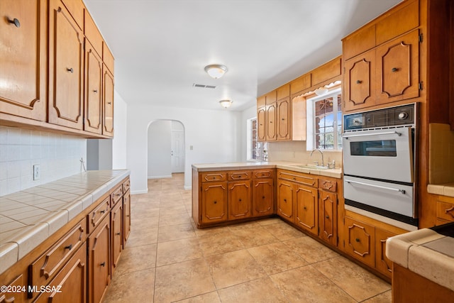 kitchen with backsplash, kitchen peninsula, white oven, and light tile patterned flooring