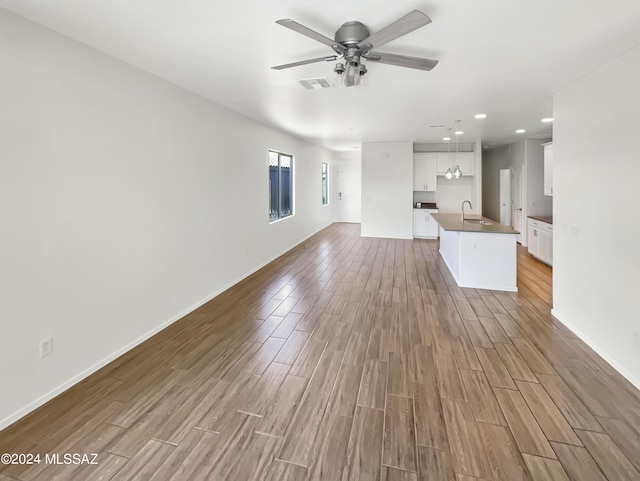 unfurnished living room featuring a sink, a ceiling fan, baseboards, visible vents, and light wood-style floors