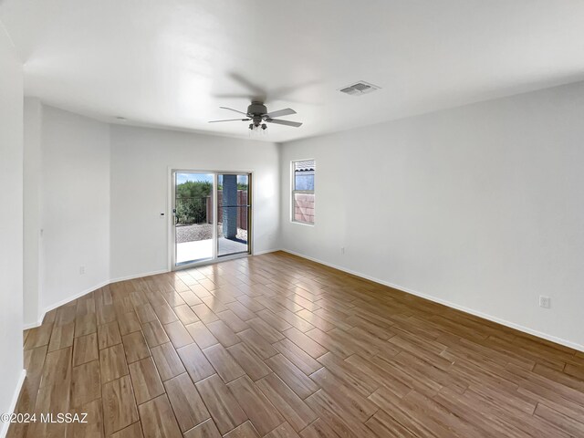 empty room featuring dark wood-type flooring, visible vents, baseboards, and a ceiling fan