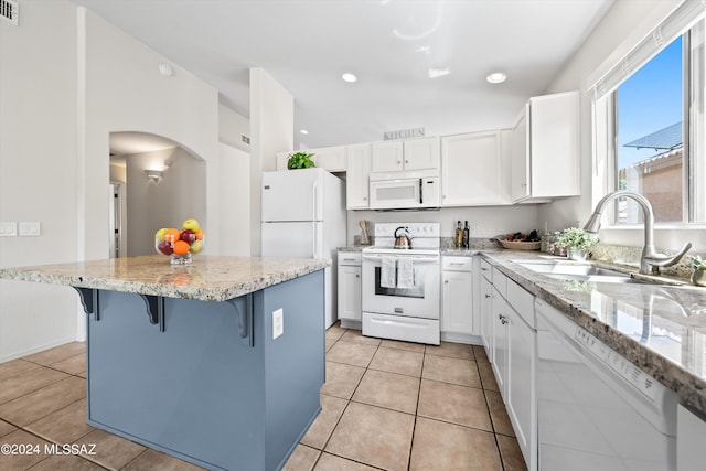 kitchen featuring white appliances, light stone counters, white cabinetry, sink, and a kitchen bar