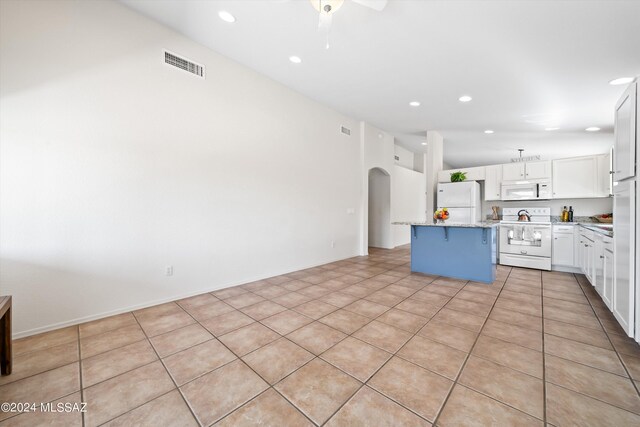 kitchen featuring white appliances, a kitchen bar, a center island, ceiling fan, and white cabinets