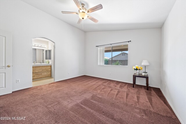 unfurnished bedroom featuring dark colored carpet, lofted ceiling, ensuite bathroom, and ceiling fan