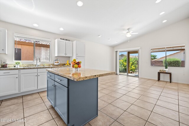 kitchen with light tile patterned floors, a kitchen island, ceiling fan, lofted ceiling, and white cabinets