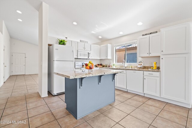 kitchen featuring white cabinetry, white appliances, a center island, light stone countertops, and lofted ceiling