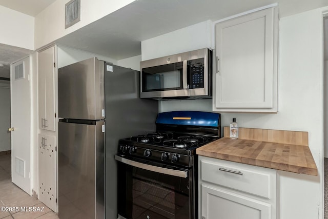 kitchen with stainless steel appliances, light tile patterned floors, white cabinets, and wood counters