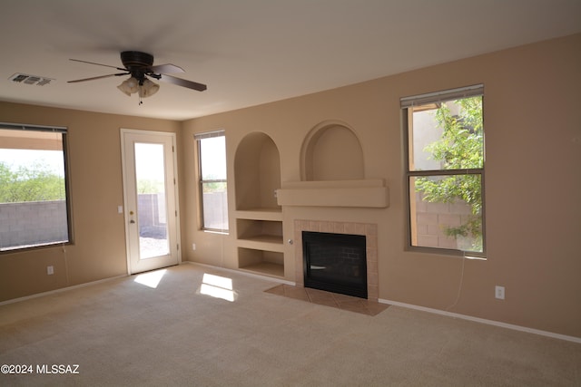 unfurnished living room featuring a tiled fireplace, light carpet, a healthy amount of sunlight, and ceiling fan