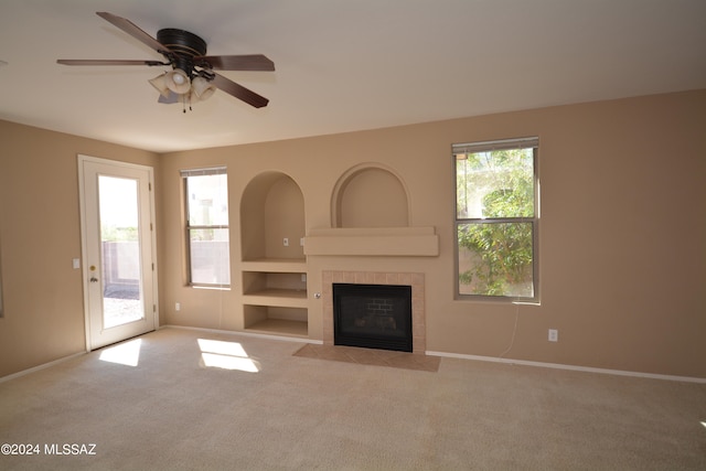 unfurnished living room with a tiled fireplace, light carpet, a healthy amount of sunlight, and ceiling fan