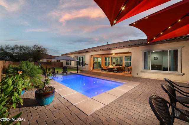 pool at dusk with a patio area and a hot tub