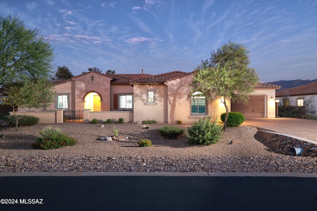 mediterranean / spanish home with fence, a tile roof, stucco siding, decorative driveway, and an attached garage