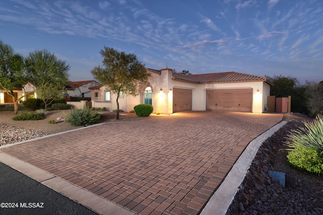 mediterranean / spanish-style house featuring stucco siding, a tiled roof, decorative driveway, and a garage