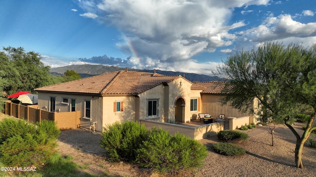 rear view of property with fence, a mountain view, a tile roof, and stucco siding