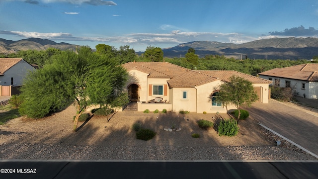 mediterranean / spanish-style home featuring an attached garage, a mountain view, a tiled roof, decorative driveway, and stucco siding