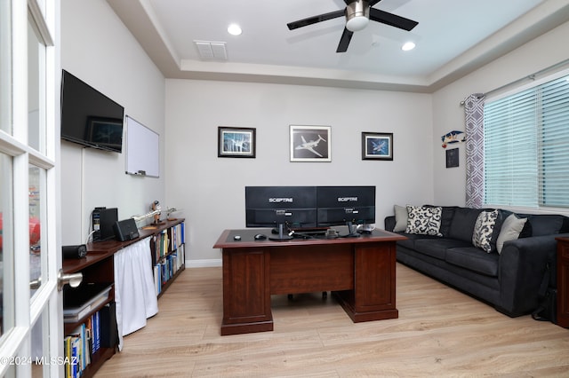 home office with a raised ceiling, ceiling fan, and light hardwood / wood-style flooring