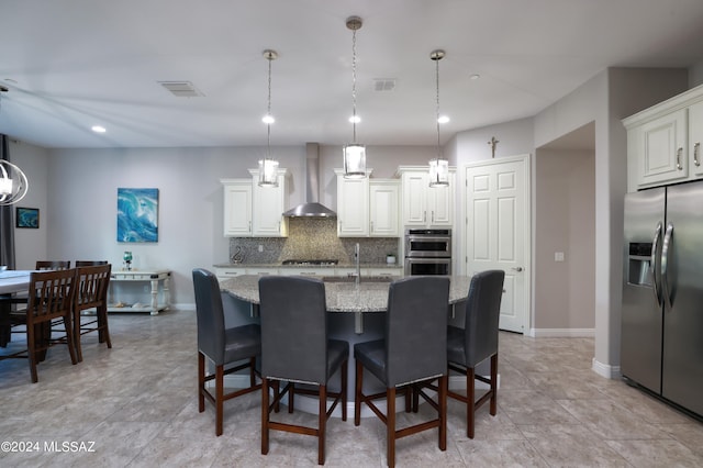 kitchen featuring visible vents, backsplash, stainless steel appliances, wall chimney exhaust hood, and light stone countertops