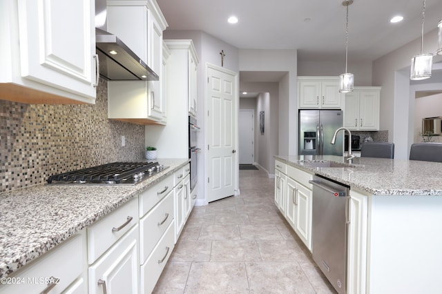 kitchen with wall chimney range hood, an island with sink, stainless steel appliances, white cabinetry, and a sink