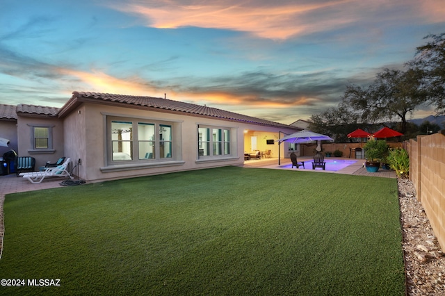 back house at dusk with a yard and a patio area