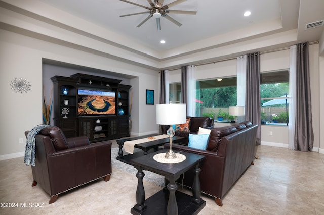 living room with visible vents, ceiling fan, baseboards, and a tray ceiling