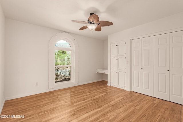 unfurnished bedroom with light wood-style floors, ceiling fan, baseboards, and multiple closets