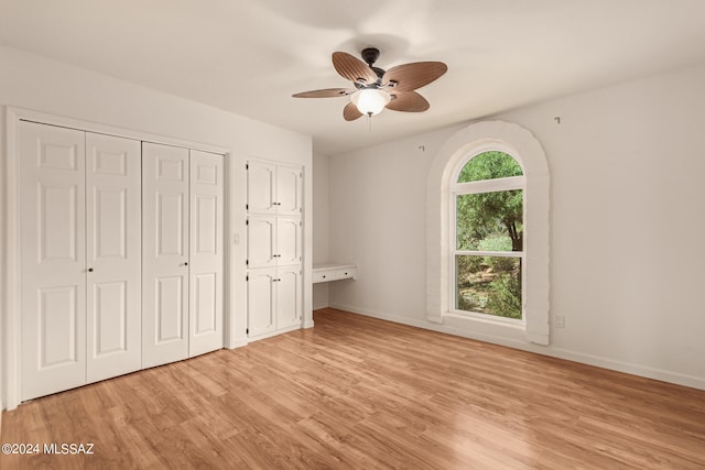 unfurnished bedroom with baseboards, two closets, a ceiling fan, and light wood-style floors