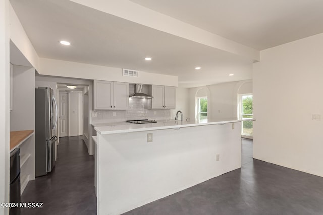 kitchen featuring finished concrete flooring, visible vents, backsplash, freestanding refrigerator, and wall chimney range hood