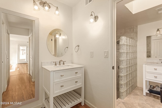 bathroom featuring vanity, a tile shower, a skylight, and hardwood / wood-style floors